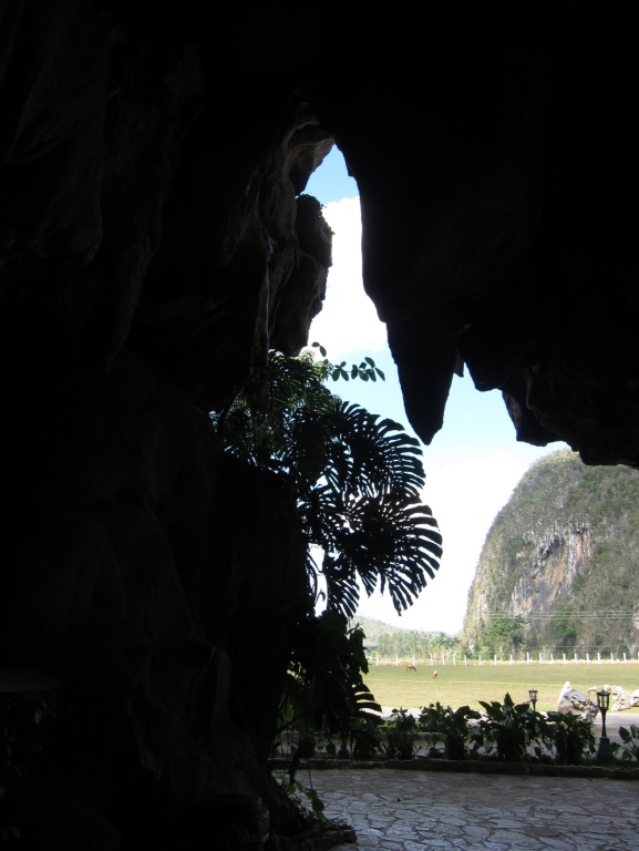 black cave surrounding small opening with blue sky & magote in distance
